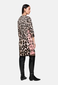 Leopardenmusterkleid mit einem rosa Blumenmuster auf einer Seite, aus weichem Stoff, dreiviertellange Ärmel und knöchellange Silhouette. Schwarze kniehohe Stiefel.