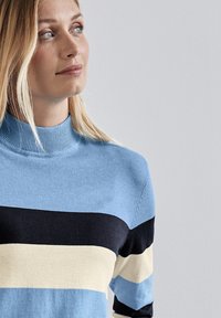 Gestreifter Pullover in hellblau, marineblau und cremefarben, mit einem gerippten hohen Kragen und weichem Material. Nahaufnahme des Oberkörpers.