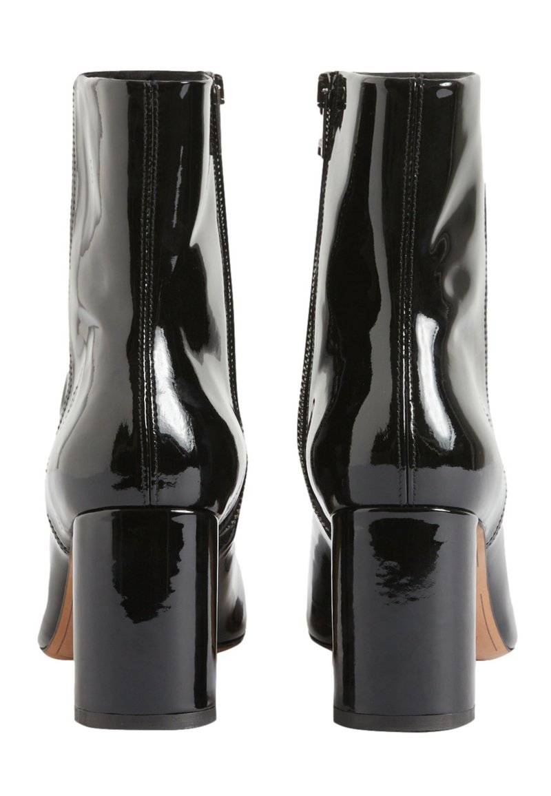 Botas de tobillo en charol negro con un alto tacón cuadrado, cremalleras laterales y una textura suave y brillante. Diseño minimalista sin patrones visibles.