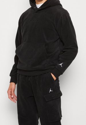 Mann trägt schwarzen Air Jordan Fleece-Hoodie mit Kängurutasche und passende schwarze Cargo-Hosen mit gestickten Jumpman-Logos.