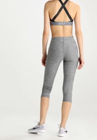 Szare legginsy sportowe o dopasowanym kroju, o długości 3/4 i teksturowanej tkaninie. Posiadają czarny detal z logo na dolnej części nogawki i są zestawione z szarymi butami.