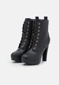 Botines negros de tacón alto con cierre de cordones en la parte delantera, ojales dorados y un panel lateral con patrón texturizado. Material de cuero liso.