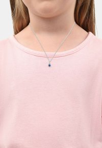 Collana in argento con ciondolo a forma di cerchio in pietra blu, indossata su una maglietta rosa chiaro a maniche corte con scollatura rotonda.