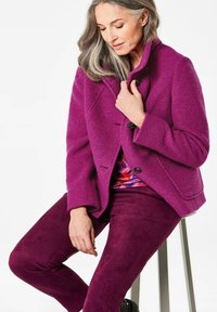 Paarse wollen blendjas met een hoge kraag, knoopsluiting en gestructureerde afwerking, gecombineerd met bijpassende suede-achtige broeken in dezelfde tint.