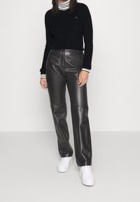 Czarny prążkowany sweter zestawiony z wysokimi, błyszczącymi czarnymi spodniami skórzanymi i białymi trampkami. Prosty design, teksturowany materiał i neutralne kolory.