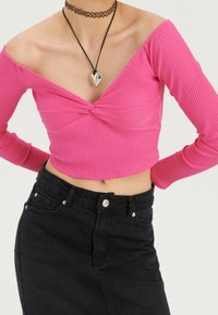 Ljusröd ribbad kort topp med off-shoulder design, tvistad frontdetalj, i kombination med en högmidjad svart denimkjol och en chokerhalsband.