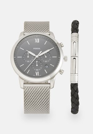 Montre en maille acier inoxydable argenté avec un cadran gris, des chiffres romains, et un bracelet en cuir tressé noir doté d'un fermoir en argent.