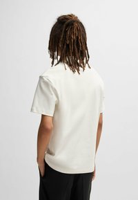 Beige Kurzarmhemd mit entspannter Passform, glatter Textur und rundem Halsausschnitt, von hinten betrachtet.
