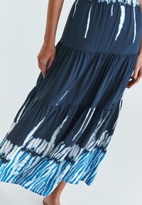 Larga falda de capas en color marino, hecha de un tejido suave, con un patrón de teñido anudado que presenta rayas azules y blancas. Cintura elástica para mayor comodidad.