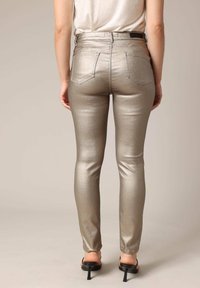 Metaalachtige zilveren skinny jeans met een hoge taille, vijf zakken en een gladde, glanzende textuur. Gekoord met zwarte haksandalen.