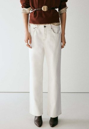 Femme portant un jean blanc taille haute à jambes larges avec une ceinture marron, un pull marron par-dessus une chemise à carreaux, et des bottines marron pointues.