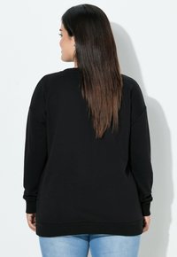 Černá oversize mikina s dlouhými rukávy, kulatým výstřihem a žebrovanými manžetami a lemem. Měkká tkanina, uvolněný střih, žádné viditelné vzory.