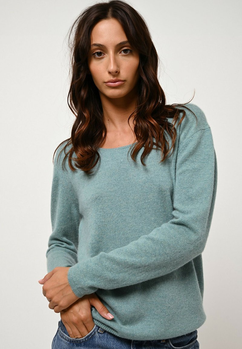 Turquoise langetermijnsweater met lange mouwen van zacht, textuurstof met een relaxte pasvorm. Heeft een ronde hals en ribgebreide manchetten, gedragen over denim.