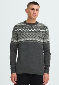 Grauer Strickpullover mit gemusterter Borte in dunkelgrün und weißen geometrischen Designs. Hat einen runden Ausschnitt und lange Ärmel.