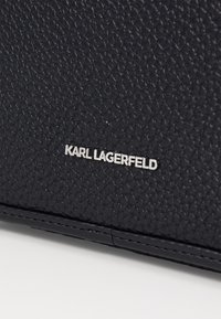 Matériau en cuir noir texturé avec un logo embossé portant la mention "KARL LAGERFELD" en argent. Le design inclut de délicates coutures.