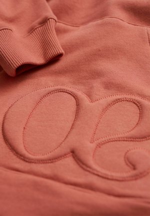 Perzikkleurige sweatshirt met een gestructureerd, verhoogd logo in een zachte stof, voorzien van ribbels aan de mouwen en gladde oppervlakdetails.