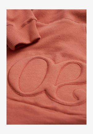 Perzikkleurige sweatshirt met een gestructureerd, verhoogd logo in een zachte stof, voorzien van ribbels aan de mouwen en gladde oppervlakdetails.