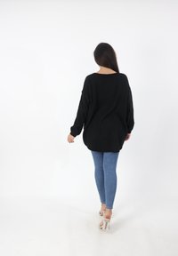 Zwarte oversized trui met lange mouwen, gebreide structuur en een ronde halslijn, gecombineerd met blauwe skinny jeans en transparante sandalen met hak.