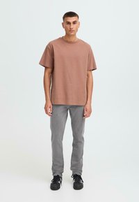 Camiseta de algodón marrón con mangas cortas, combinada con jeans de mezclilla grises y zapatillas negras. Diseño sencillo, corte relajado.