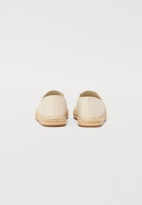 Béžové espadrilky s pletenou jutovou podrážkou, hladkým svrškem a jemným embosovaným vzorem loga na zadní straně. Design na obutí, zaoblená špička.