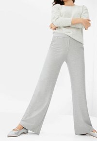 Pantalon large gris clair en tissu doux et extensible, avec une ceinture lisse et des détails de poches subtils. Associé à des ballerines argentées brillantes.