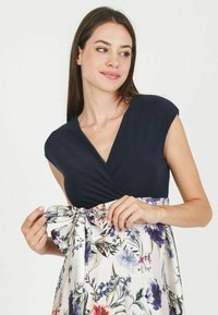 Robe florale avec un corsage bleu marine et une jupe blanche ornée de motifs floraux colorés ; détail de lien à la taille ; texture de tissu lisse.