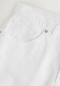 Close-up af hvide denimjeans, der viser forreste lomme, lille møntlomme, bæltestrop og metalnitte-detalje.