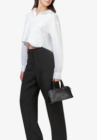 Sort læderhåndtaske med guldbeslag, struktureret form og korte håndtag. Modellen har en cropped hvid skjorte og sorte bukser på.