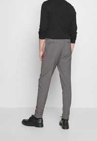 Grå byxor med en texturerad tyg, slim fit, och bakfickor, i kombination med svarta skor och en långärmad svart skjorta.