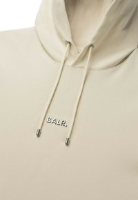 Beige hættetrøje med stor hætte, snore og et lille sølvlogo "BALR." foran. Blød stoftekstur med minimalistisk design.