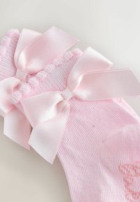 Chaussettes de bébé roses douces avec de délicats nœuds en satin et des bords froncés sur un fond clair.