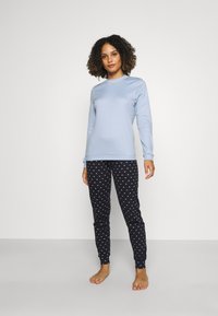 Lichtblauw langemouwen top gecombineerd met zwarte pyjamabroek met witte hartpatronen. Zachte, elastische stof; aansluitend ontwerp.