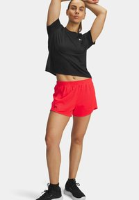 Zwarte sportieve top met korte mouwen en een ronde hals, voorzien van een logo, gecombineerd met felrode mesh korte broeken met een elastische tailleband.