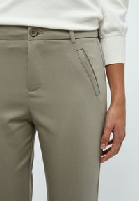 Pantaloni beige su misura realizzati in un tessuto liscio, con una tasca frontale e una chiusura con bottone in vita. Design semplice ed elegante.