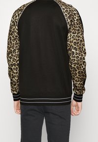 Felpa nera con maniche a stampa leopardo, dotata di polsini e orlo a coste con strisce bianche. Texture liscia con motivi a contrasto.