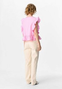 Top rosa con volant e orlo a peplum, abbinato a pantaloni larghi beige chiaro. Il tessuto appare liscio e con una consistenza morbida.