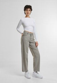 Jeans de pierna ancha gris claro con cinco bolsillos y cierre de botón, combinados con una camiseta ajustada blanca de manga larga y zapatillas blancas.