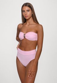 Lichtroze bandeau bikini top met gedraaid stof en metalen accent, gecombineerd met een hoge taille bikini broek in dezelfde kleur. Katoene textuur.