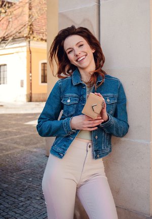 Denim jacket with button details, light green top, and beige high-waisted pants; holding a tan leather wallet with a metal accent.