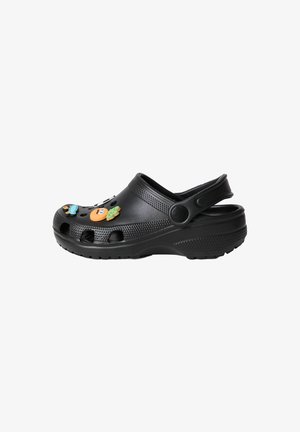 Sabot noir avec embout perforé, bride de talon et breloques colorées en forme de fruits et de personnages attachées sur le dessus.