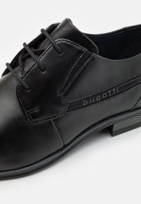 Black leather dress shoe featuring a smooth finish, lace-up design, and subtle branding on the side with a textured sole for grip.