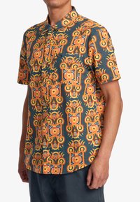 Camicia a maniche corte con un vivace e intricato motivo geometrico arancione e blu su uno sfondo scuro, realizzata in tessuto leggero.