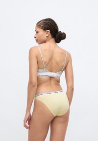 Γκρι σουτιέν bralette με ρυθμιζόμενες τιράντες και λευκή ελαστική ταινία· συνδυασμένο με κίτρινο εσώρουχο με λευκή ζώνη στη μέση. Μαλακό ύφασμα, απλός σχεδιασμός.