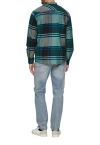 Gespiegelde flanellen shirt in teal, zwart en grijs, met lange mouwen en een klassieke kraag, gecombineerd met lichtblauwe vervaagde jeans en witte sneakers.