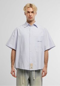 Camicetta a maniche corte a righe in blu chiaro e bianco. Presenta una tasca sul petto con del testo, una vestibilità comoda e un'etichetta tessuta all'orlo.