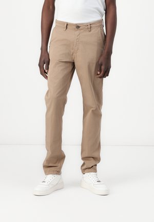 Beige Baumwollhosen mit geradem Schnitt, ausgestattet mit einem Knopfverschluss, Fronttaschen und einer glatten Textur. Tragen mit weißen Sneakers.