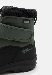 Zeleni zimski čizm koji imaju crni gumeni potplat, s fluffy crnim ovratnikom i čičak trakom. Jack Wolfskin logo vidljiv sa strane.
