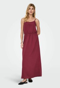 Burgundia maksikleid õhukeste rihmadega, elastse vöökohtadega, pehme kangaga ja laia siluettiga. Kantud mustade lamedate kingadega.