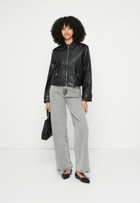 Melnas mākslīgās ādas bomber tipa jaka ar rāvējslēdzēju, ar priekšējām kabatām, valkāta virs gaiši pelēniem, platām džinsiem un melnām kurpēm bez papēžiem, ar mazu melnu somiņu.