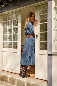 Femme en robe en denim et bottes à fleurs debout dans une porte, tenant la porte ouverte, regardant par-dessus son épaule.
